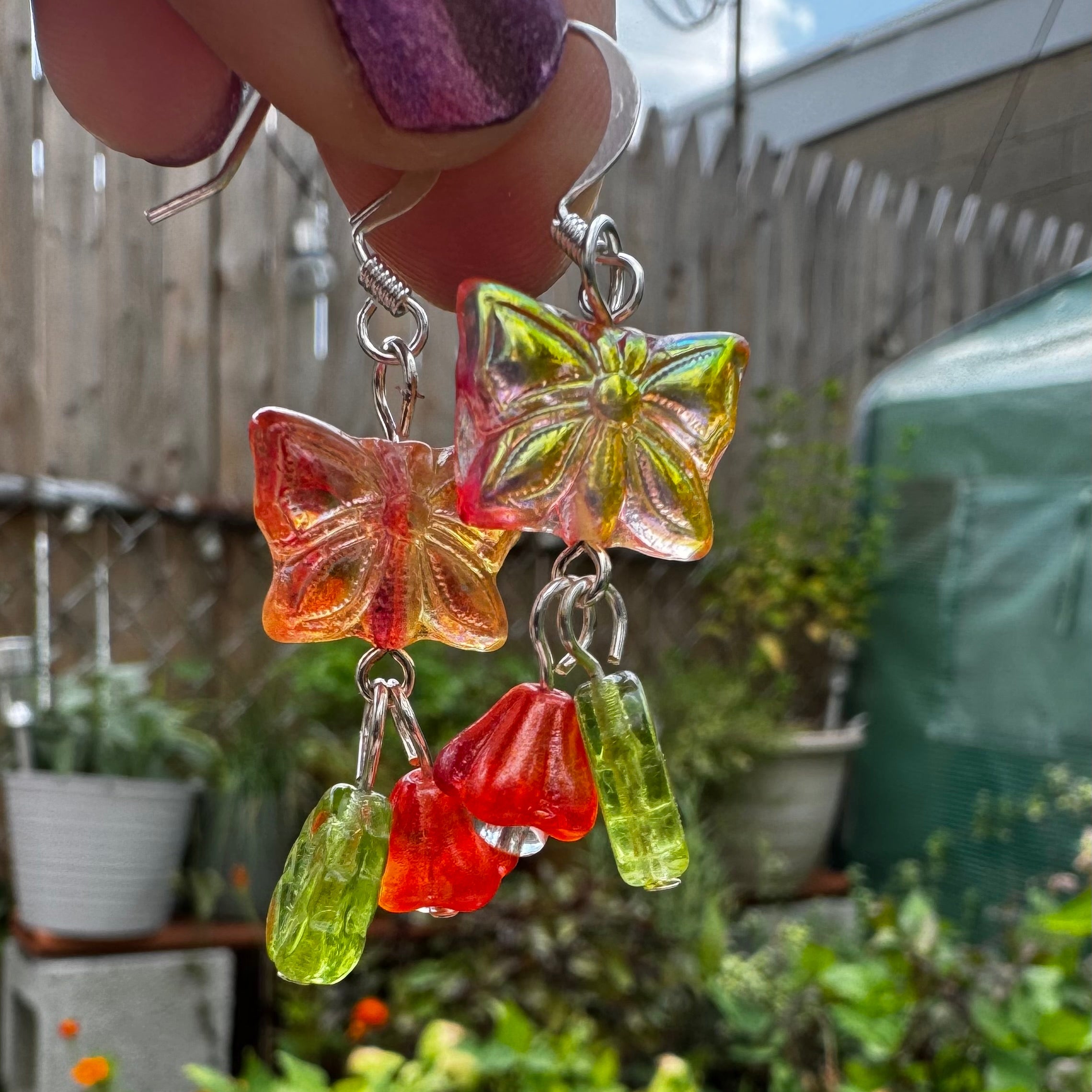 Colorful butterfly-shaped earrings held up in front of a garden setting.